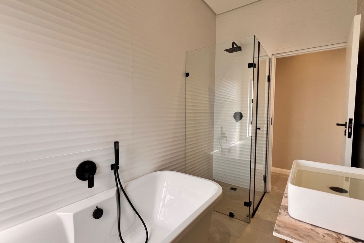 Modern bathroom featuring a sleek freestanding bathtub, glass-enclosed shower with matte black fixtures, and a contemporary vessel sink on a stone vanity.