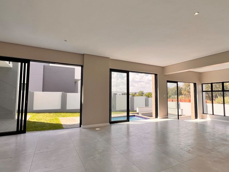 Spacious open-plan living area featuring large format floor tiles, recessed lighting, and multiple sliding glass doors providing seamless access to the garden and pool area.