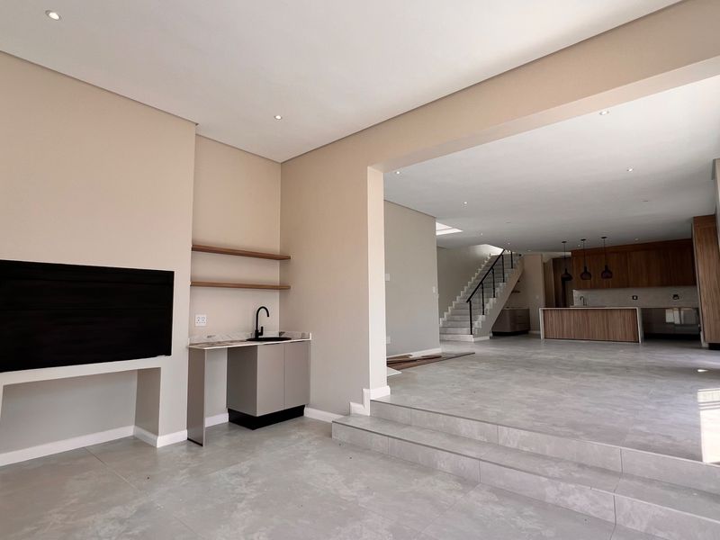 Spacious open-plan living area featuring a modern kitchen with island, wet bar, tiled floors, and a staircase leading to the upper level.
