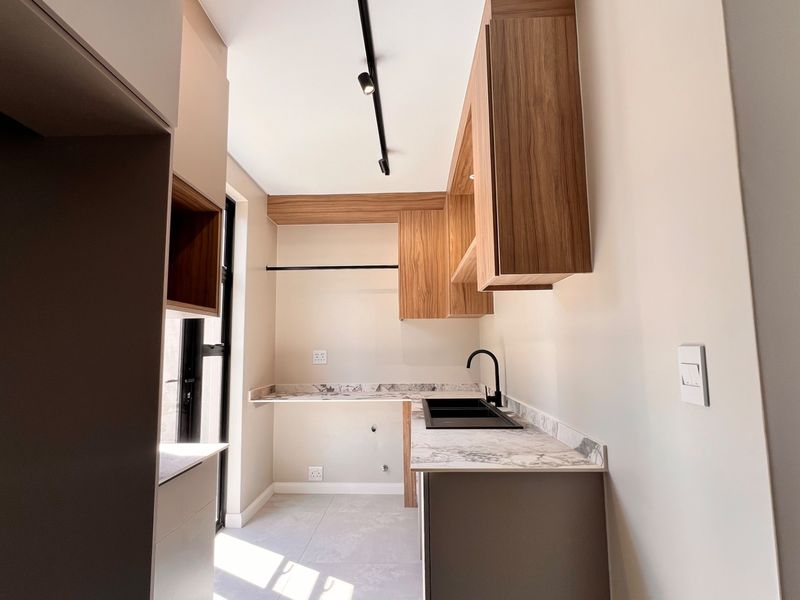 Modern scullery featuring sleek wood-finish cabinetry, stone countertops, a black sink with matching tapware, and contemporary track lighting.