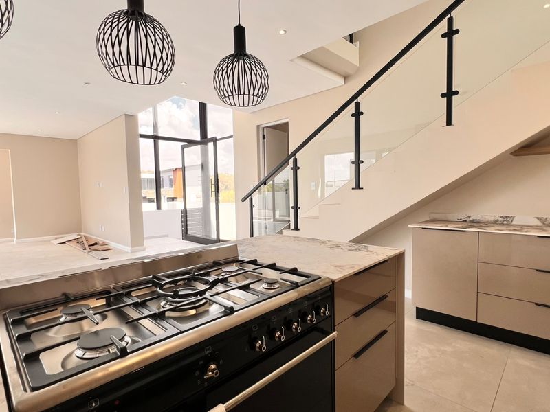 Modern open-plan kitchen and living area featuring a gas stove, stone countertops, sleek cabinetry, and a contemporary staircase with a glass balustrade.