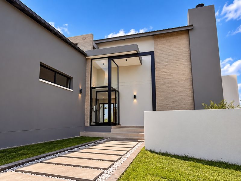 A striking modern front facade featuring a glass-enclosed entrance, stone cladding, and a clean, minimalist design with a paved walkway.
