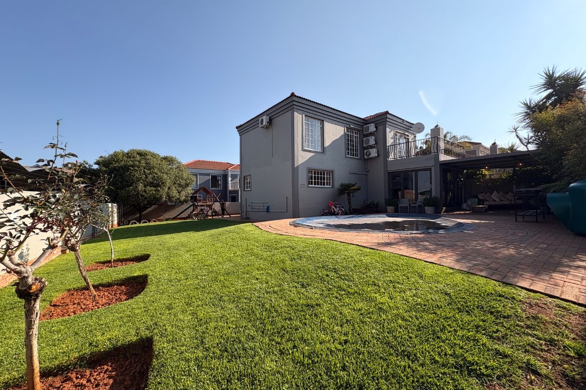 Rear view of the townhouse featuring a well-maintained lawn, paved patio area, swimming pool, and an upper-level balcony.