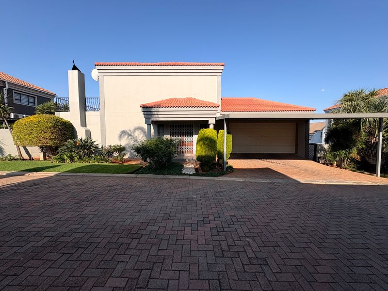 Front elevation of a townhouse featuring a paved driveway, integrated carport, garage, and terracotta tiled roof with established garden landscaping.