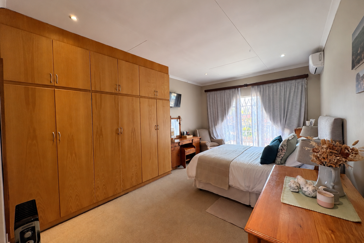 Spacious bedroom featuring extensive built-in wooden cabinetry, wall-mounted air conditioning, recessed lighting, and direct access to a balcony through a secure sliding door.