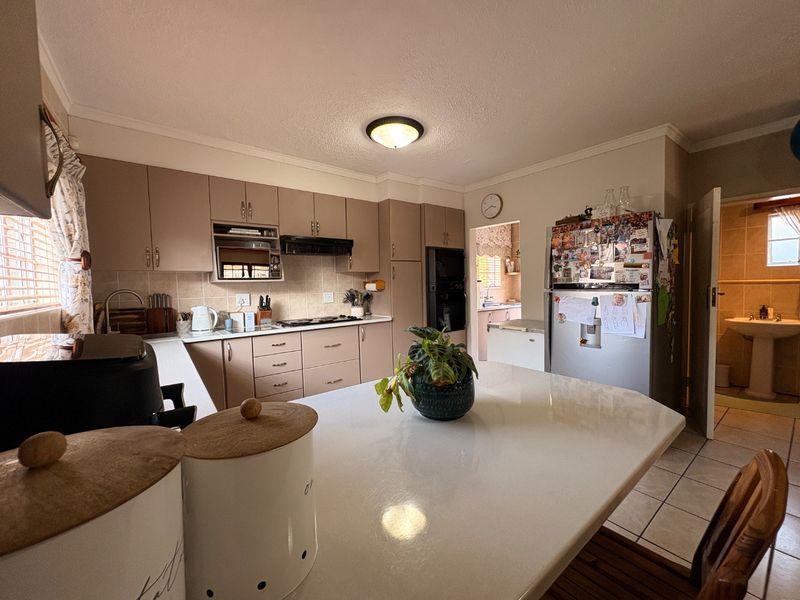 A functional kitchen featuring built-in cabinetry, a central island, and a tiled backsplash, with an adjacent scullery area visible.