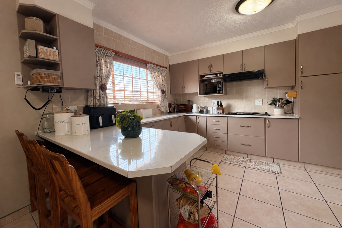 A functional kitchen featuring neutral-toned cabinetry, stone countertops, a built-in oven, and a breakfast bar area with tiled flooring.