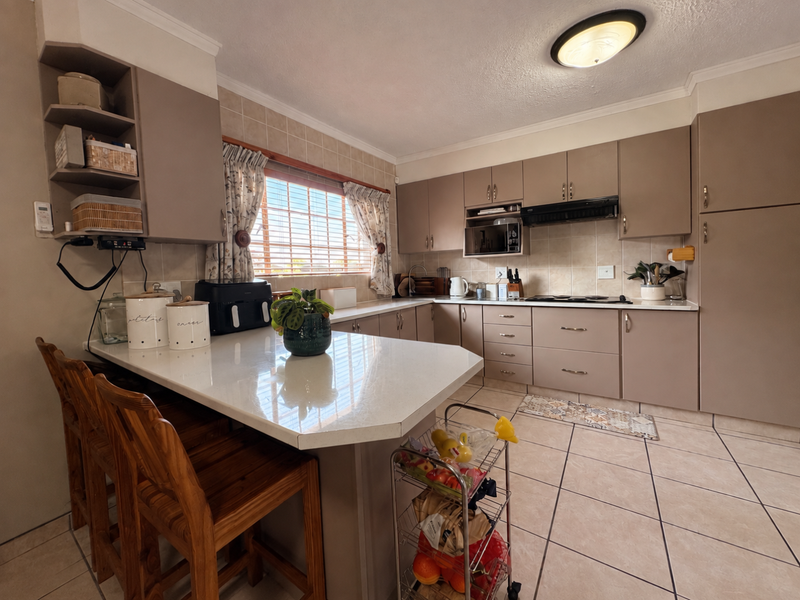 A functional kitchen featuring neutral-toned cabinetry, stone countertops, a built-in oven, and a breakfast bar area with tiled flooring.