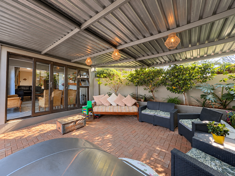 A spacious covered patio featuring a corrugated metal roof, paved flooring, and large sliding glass doors providing seamless access to the interior living area.