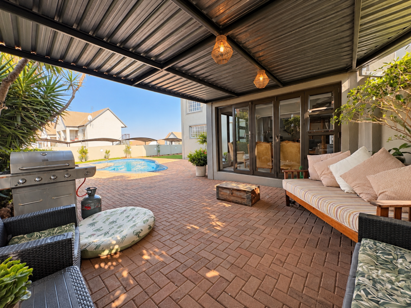A spacious covered patio featuring paved flooring and bi-fold doors, providing seamless access to the outdoor pool area.
