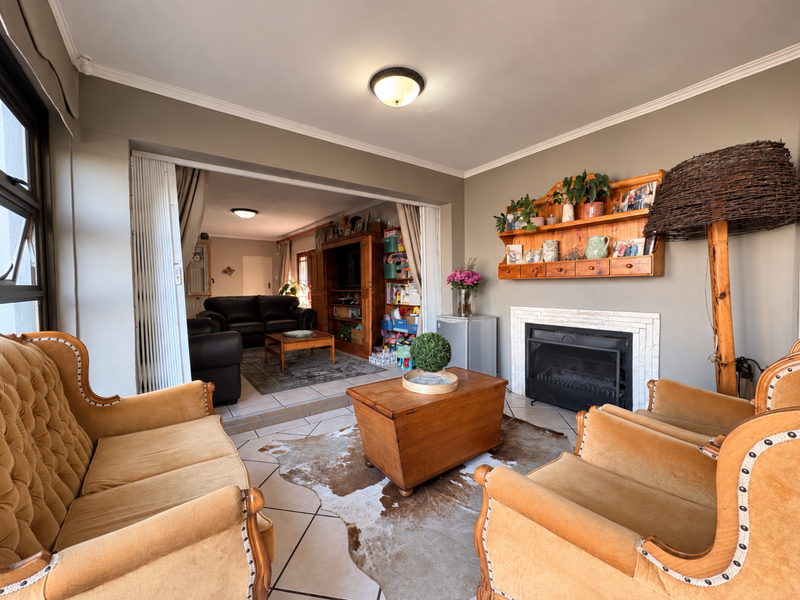 A cozy living room featuring a fireplace with a tiled surround, crown molding, and tiled flooring, connected to an adjacent living space via sliding doors.