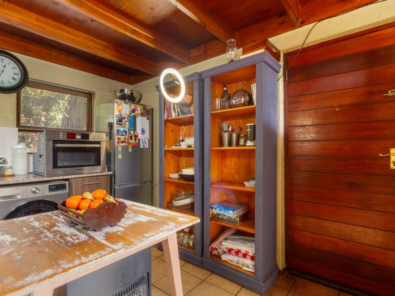 A rustic kitchen featuring exposed timber ceiling beams, tiled flooring, and built-in cabinetry with integrated oven and laundry appliance space.