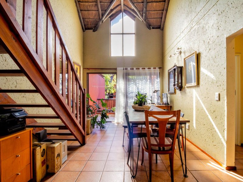 Open-plan living area featuring a double-volume thatched ceiling, exposed timber rafters, a wooden staircase, and ceramic tiled flooring with access to a patio.
