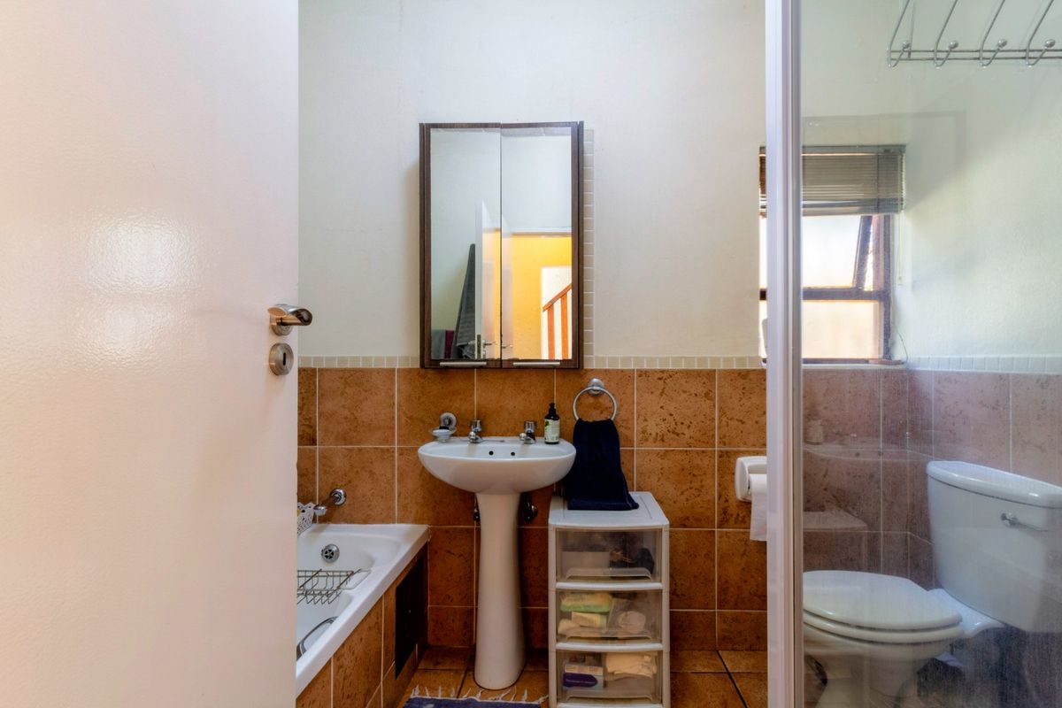 A functional bathroom featuring a pedestal basin, built-in bathtub, separate shower enclosure, and toilet with neutral tiled finishes.