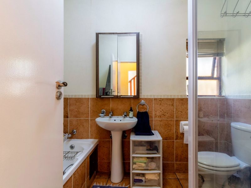 A functional bathroom featuring a pedestal basin, built-in bathtub, separate shower enclosure, and toilet with neutral tiled finishes.