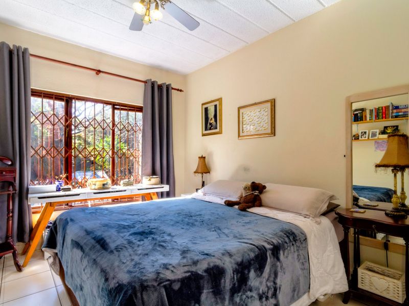 A functional bedroom featuring tiled flooring, a ceiling fan, and a window fitted with a security gate for added protection.