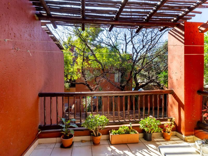 A covered balcony featuring a rustic timber pergola and balustrade, offering an outdoor space with tiled flooring and views of the surrounding trees.