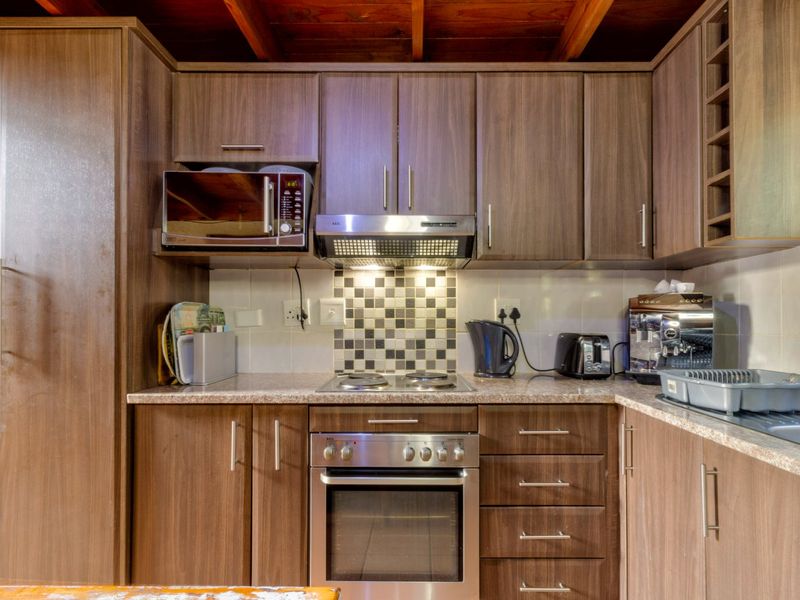 A functional kitchen featuring wood-finish cabinetry, granite-look countertops, built-in oven and hob, and a distinctive exposed timber beam ceiling.