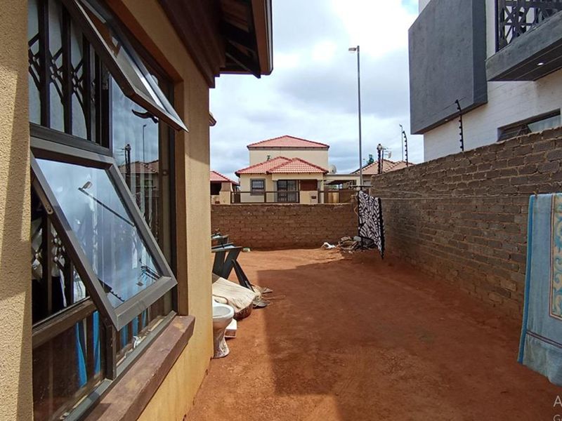 A rear exterior area featuring a brick boundary wall and a side view of the house with security-fitted windows.