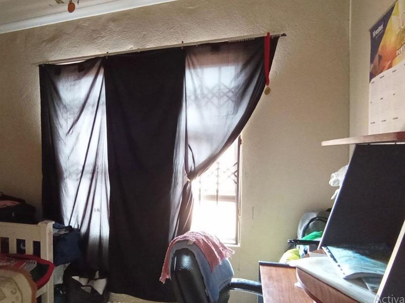 A bedroom featuring a window with a security gate, showing signs of wear on the wall finishes.
