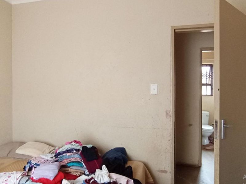 A bedroom interior featuring plain walls and a doorway leading to an adjacent bathroom area.