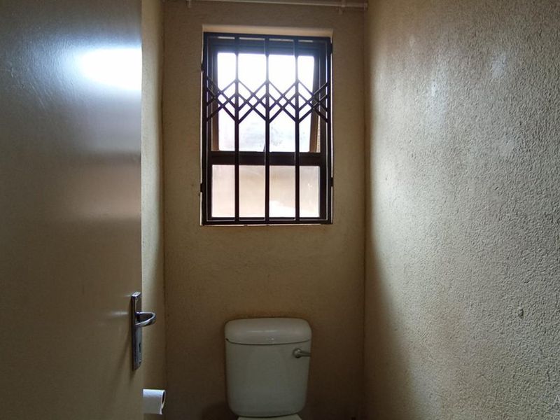 A compact bathroom featuring a standard toilet and a window with a security gate, requiring cosmetic updates to the wall finishes.