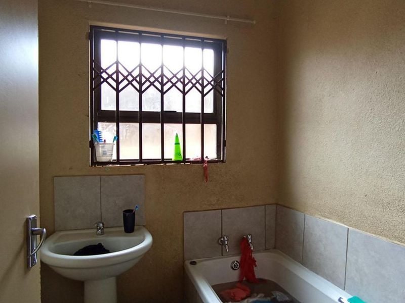 A functional bathroom featuring a pedestal basin, built-in bathtub, and a window fitted with a security gate.