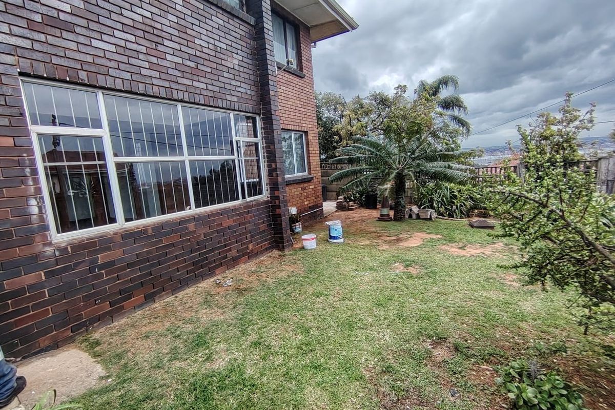 Rear view of the property featuring a face brick facade, large windows with security bars, and a garden area with lawn.