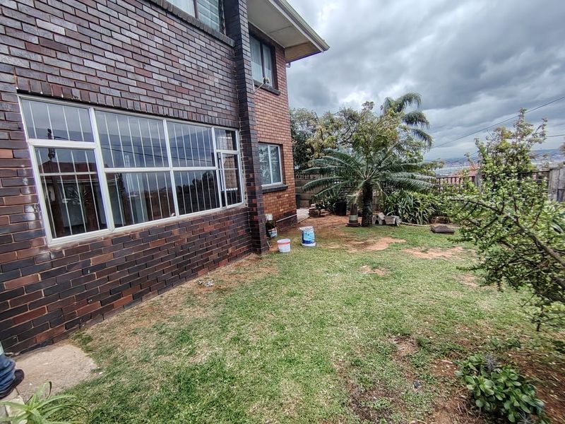 Rear view of the property featuring a face brick facade, large windows with security bars, and a garden area with lawn.