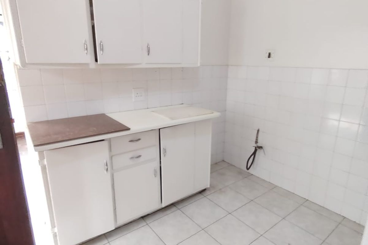 A compact, empty kitchen area featuring white built-in cabinetry, tiled splashbacks, and tiled flooring, offering a blank canvas for potential renovation.