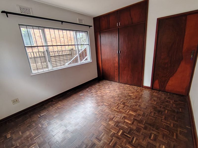 A vacant bedroom featuring classic parquet flooring, built-in wooden cabinetry, and a window fitted with security bars.