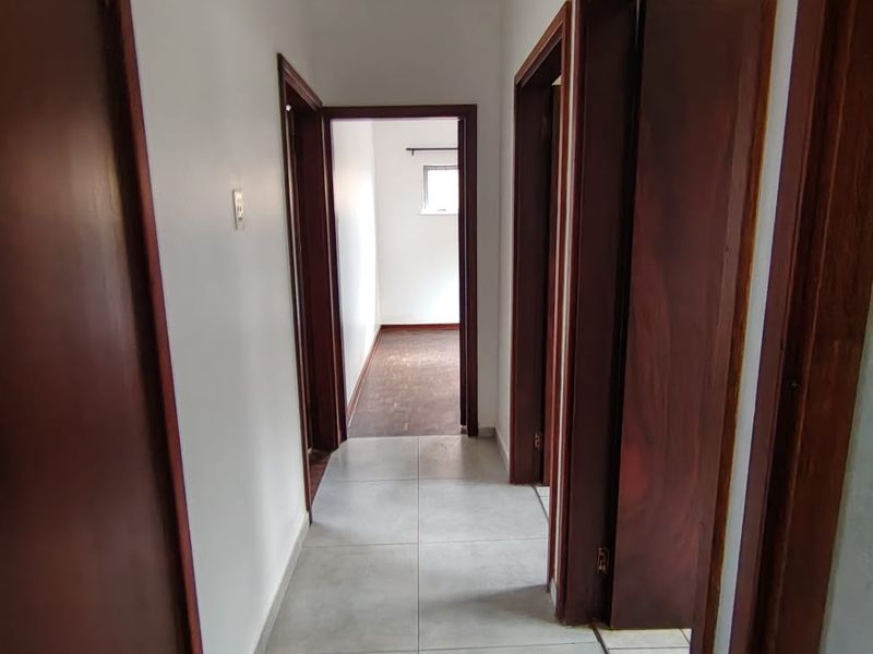 A clean, empty hallway featuring neutral floor tiles and dark wood door frames leading to adjacent rooms.