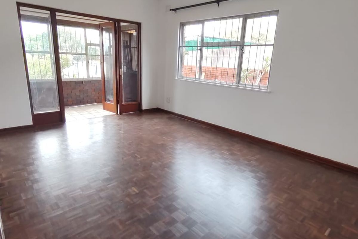 Spacious living room featuring original parquet flooring, large windows with security bars, and direct access to an adjoining patio area.