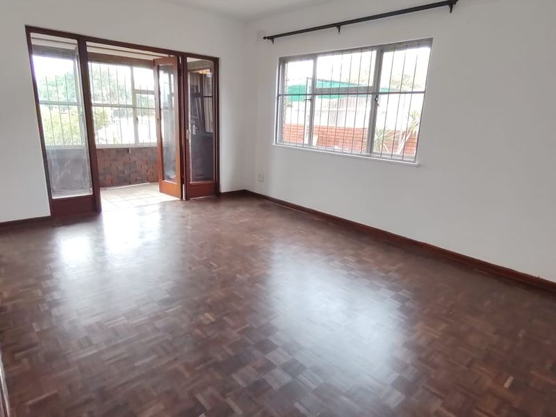 Spacious living room featuring original parquet flooring, large windows with security bars, and direct access to an adjoining patio area.