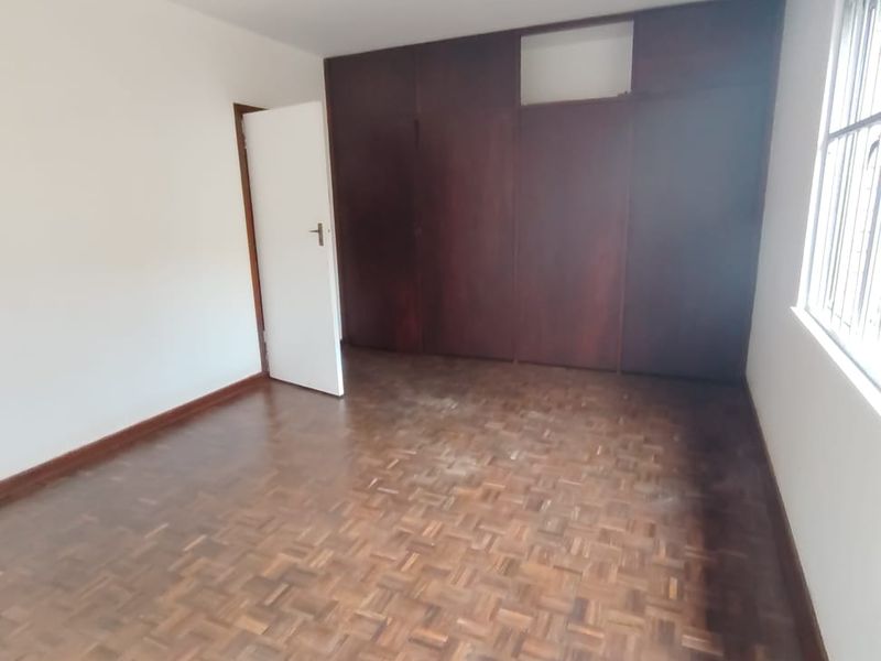 An empty bedroom featuring classic parquet flooring and dark wood built-in cupboards, offering a blank canvas for renovation or styling.