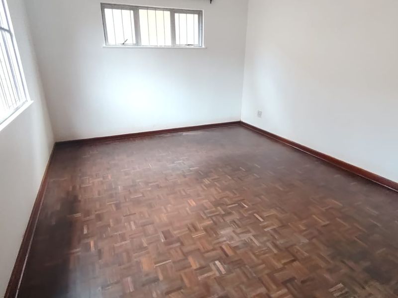 A vacant bedroom featuring classic parquet flooring, white walls, and windows fitted with security bars.