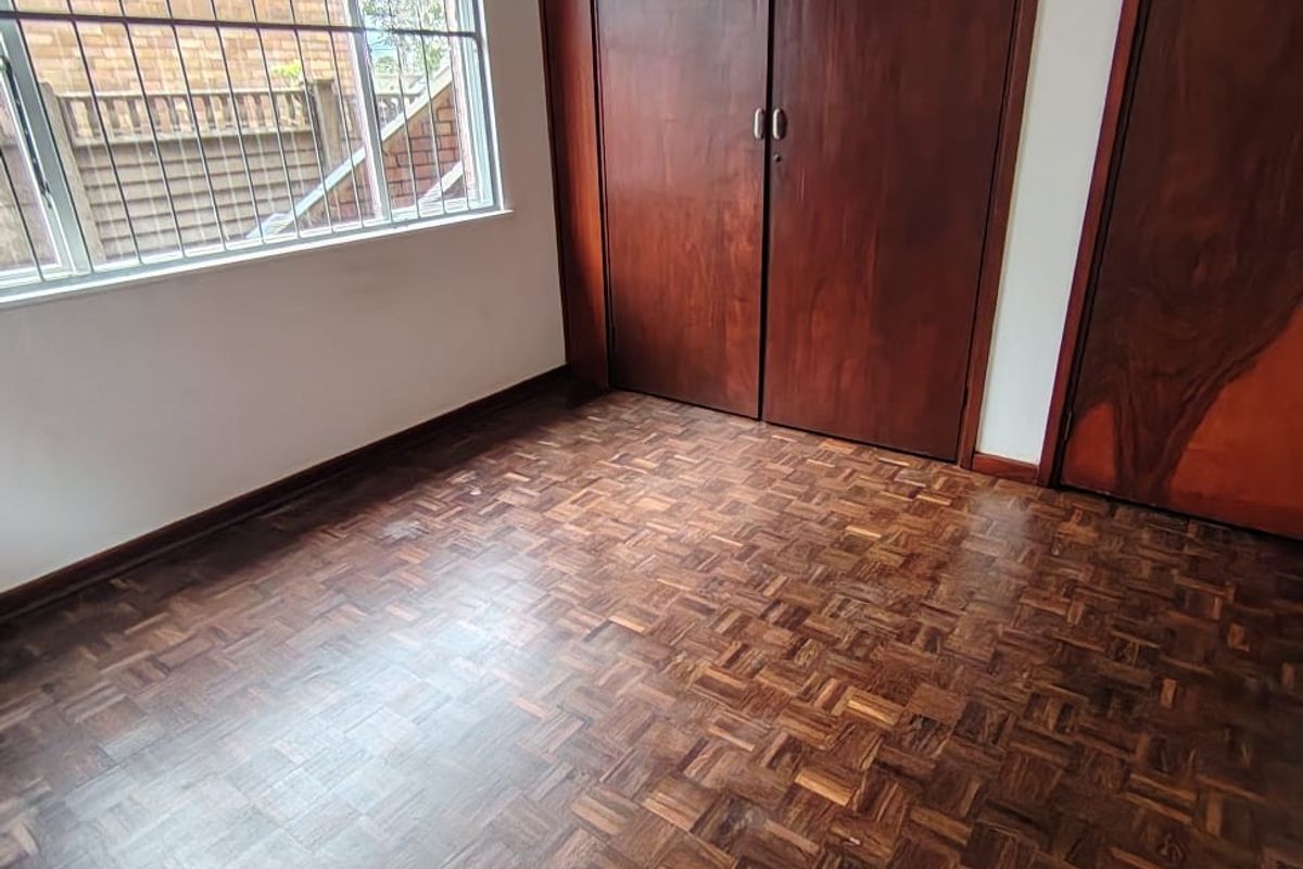 A vacant bedroom featuring classic parquet flooring, built-in wooden cabinetry, and a window fitted with security bars.