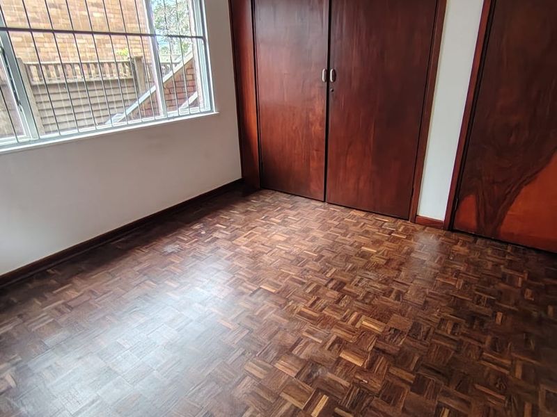 A vacant bedroom featuring classic parquet flooring, built-in wooden cabinetry, and a window fitted with security bars.