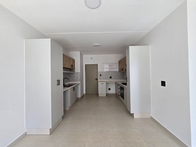 A modern, clean, and empty kitchen featuring built-in cabinetry, a hob, an oven, and a tiled backsplash, offering a neutral and functional workspace.