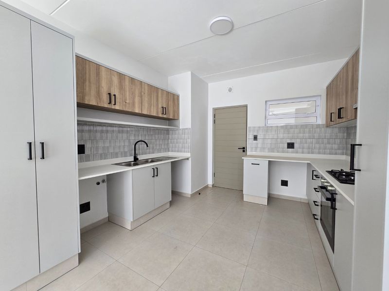 Modern kitchen featuring light wood-tone cabinetry, white countertops, tiled backsplash, built-in oven, and gas hob in a clean, contemporary layout.