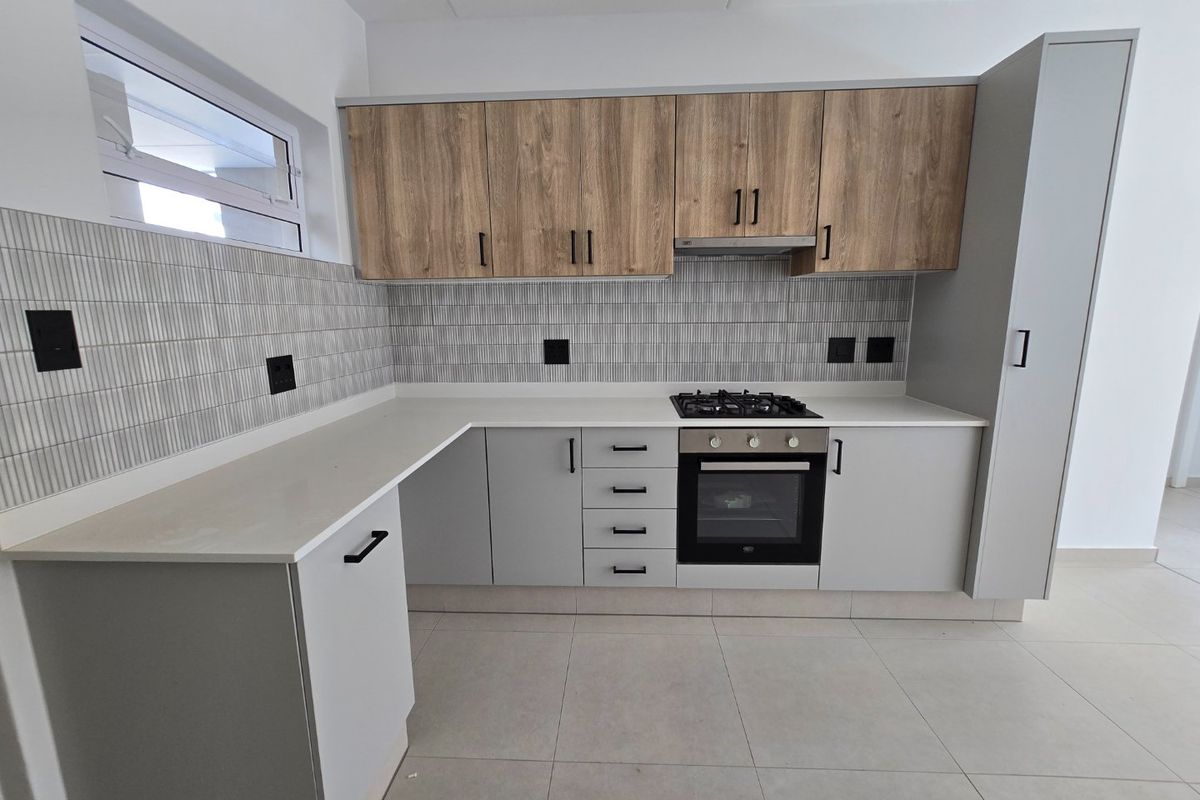 Modern kitchen featuring light grey cabinetry, wood-look upper cabinets, stone countertops, gas hob, built-in oven, and a stylish tiled backsplash.