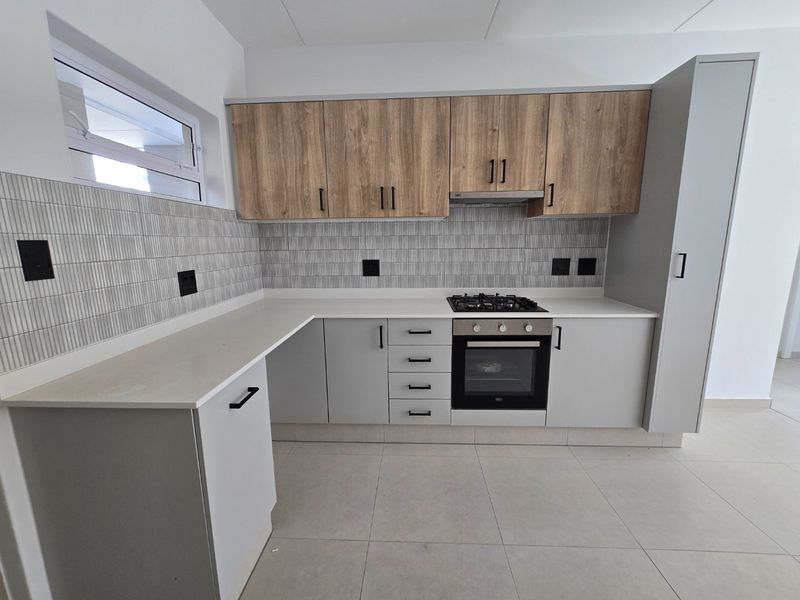 Modern kitchen featuring light grey cabinetry, wood-look upper cabinets, stone countertops, gas hob, built-in oven, and a stylish tiled backsplash.