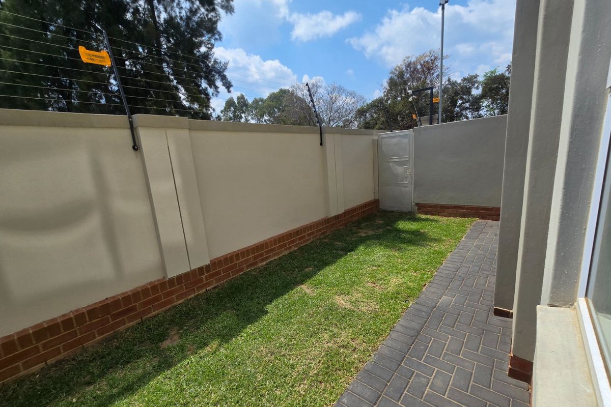 A private rear garden area featuring a well-maintained lawn, brick paved pathway, and secure perimeter wall with electric fencing.