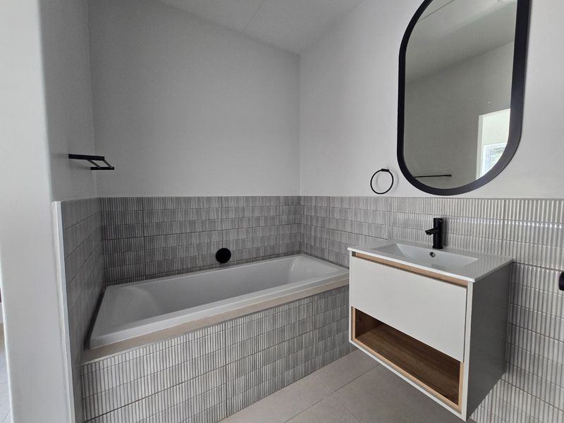 Modern bathroom featuring a built-in bathtub, wall-mounted vanity with integrated sink, contemporary black fixtures, and stylish textured wall tiling.