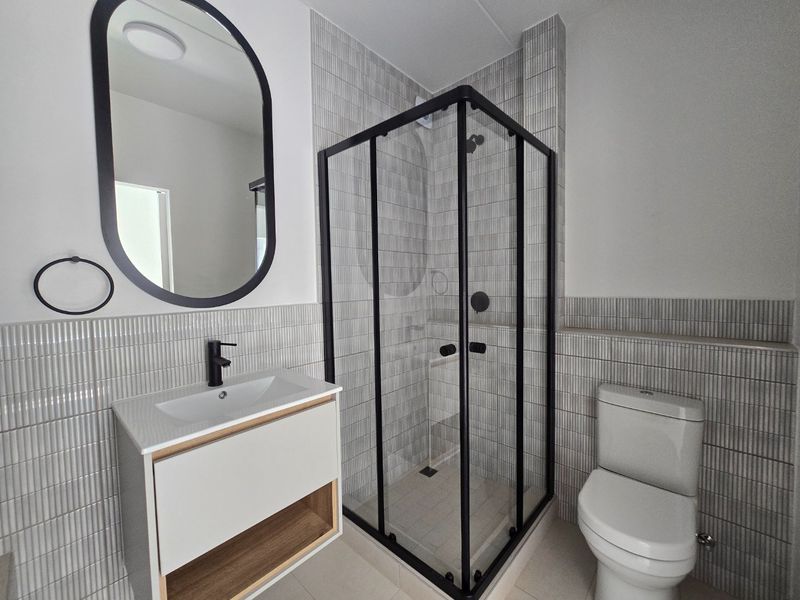 Modern bathroom featuring a sleek vanity, black tapware, a glass shower enclosure, and contemporary tiled finishes throughout.