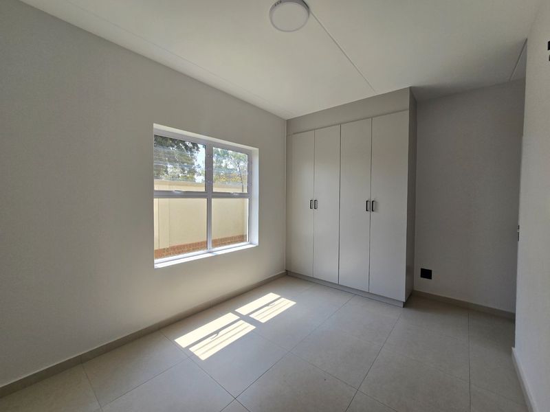 A bright, empty bedroom featuring neutral tiled flooring, clean white walls, and modern built-in cupboards.