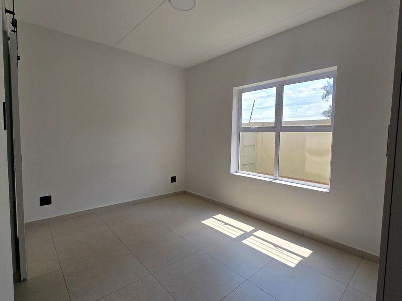 A bright, empty bedroom featuring neutral tiled flooring, a large window, and a sliding door, providing a clean and versatile space.
