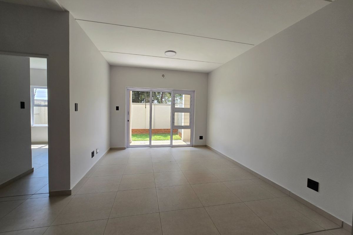 A bright, empty living area featuring neutral tiled flooring and a sliding glass door providing access to the rear garden.