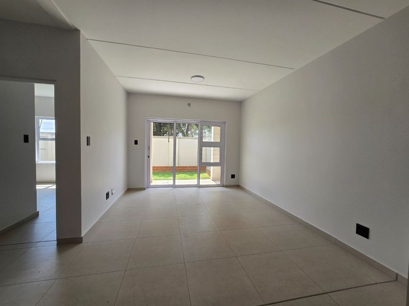 A bright, empty living area featuring neutral tiled flooring and a sliding glass door providing access to the rear garden.