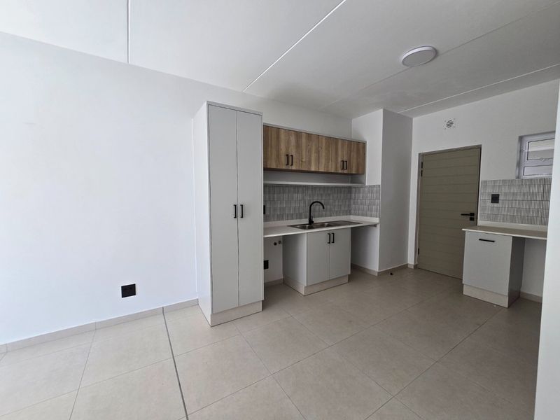 A modern, clean kitchen area featuring neutral cabinetry, tiled backsplash, and tiled flooring in an open-plan layout.